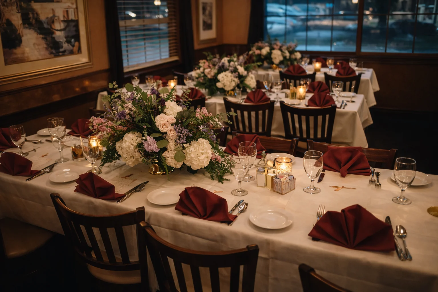 Candlelit dining room at Mirna's Café with tables set with white linens, burgundy napkins, and floral centerpieces